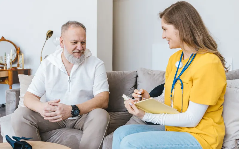 Nurse talking with an older patient at home on the couch